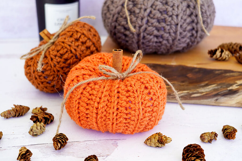 Crochet Pumpkins on and around a butcher block with a candle in the background and pinecones scattered around