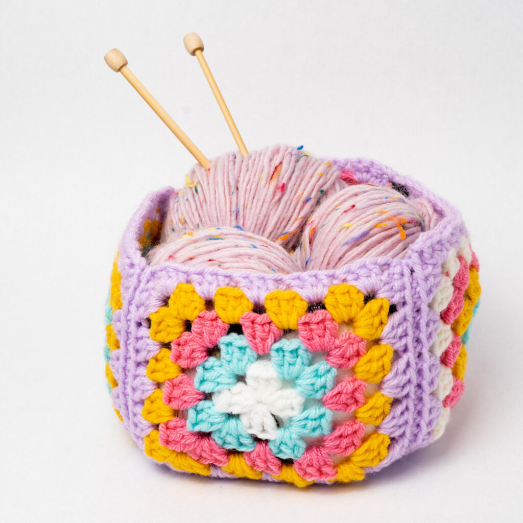 granny square basket with yarn and knitting needles in it