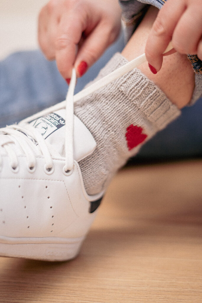 Person tying shoelaces while wearing handmade knitted heart socks in soft grey yarn.