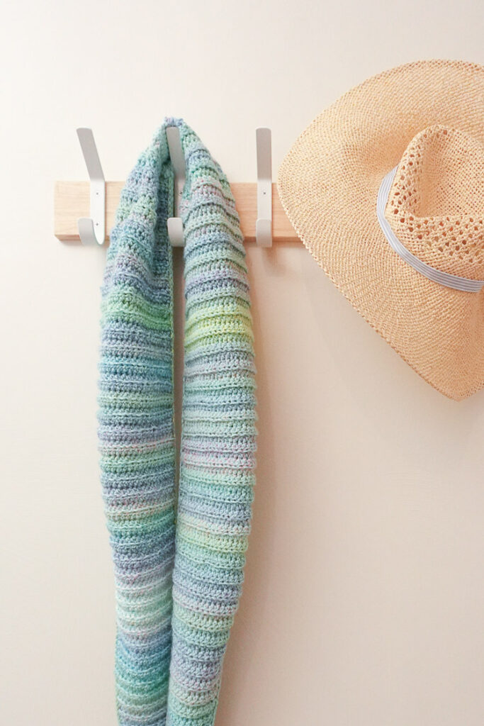 This crocheted ribbed shawl is hanging next to a stylish sun hat