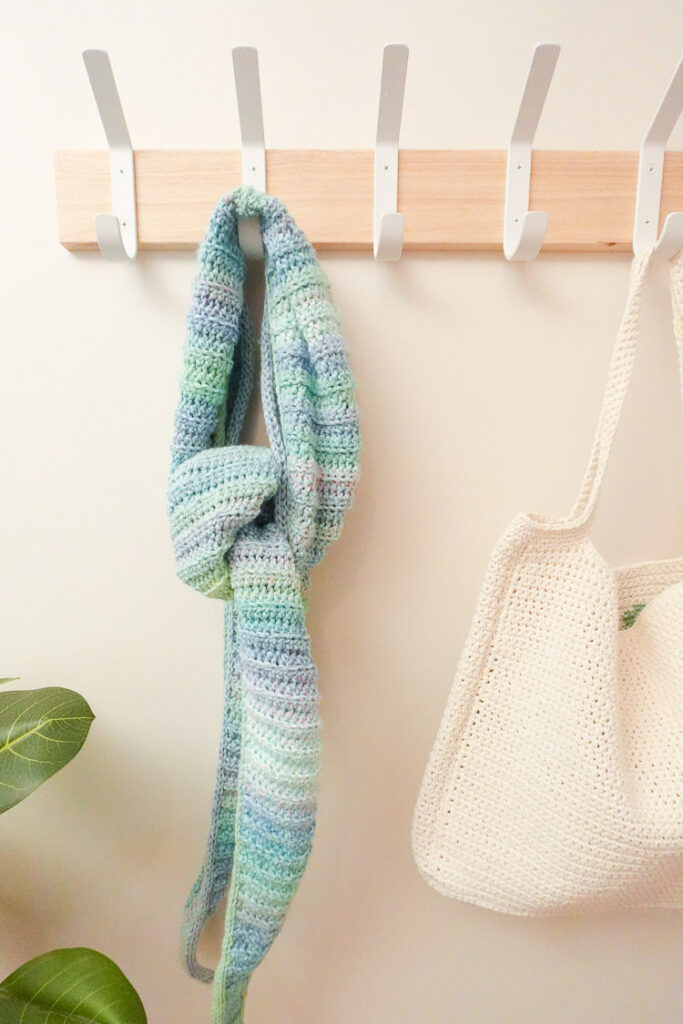 The crochet shawl is hanging from a hook next to a stylish crochet bag