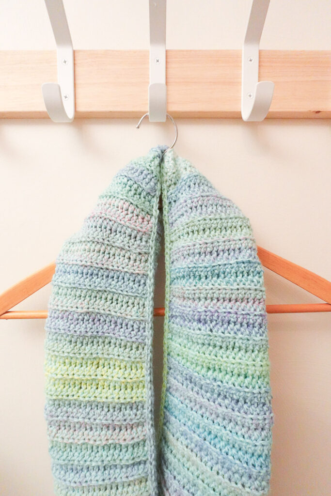 Crochet shawl hanging on a wooden hanger.