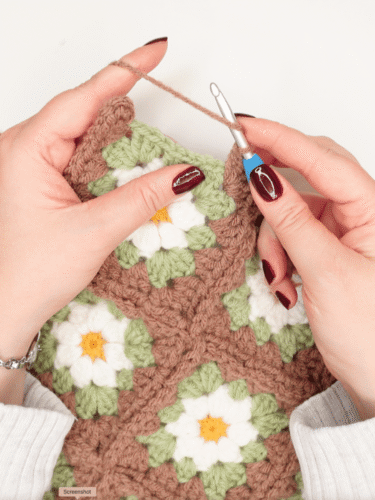 hands holding a granny square project and crochet hook