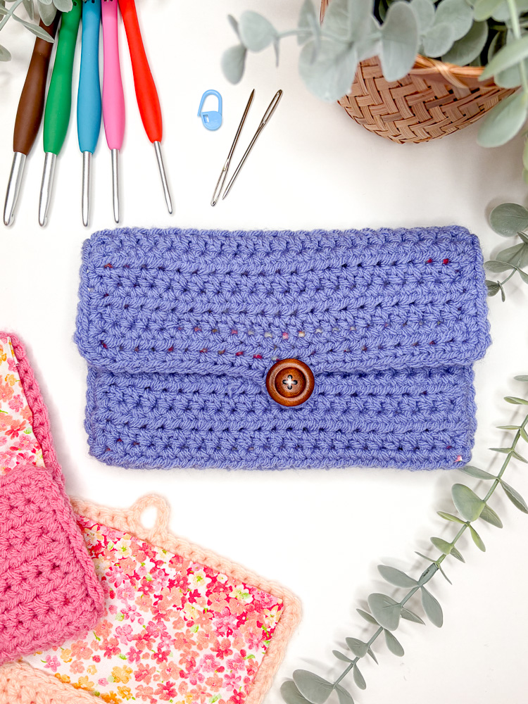 button crochet pouch arranged in a flat lay with 2 more crochet pouches showing their lining, as well as crochet hooks and notions that can be placed inside the bag