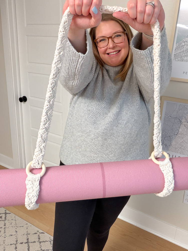 woman holding a boho crocheted yoga mat strap that is holding a yoga mat