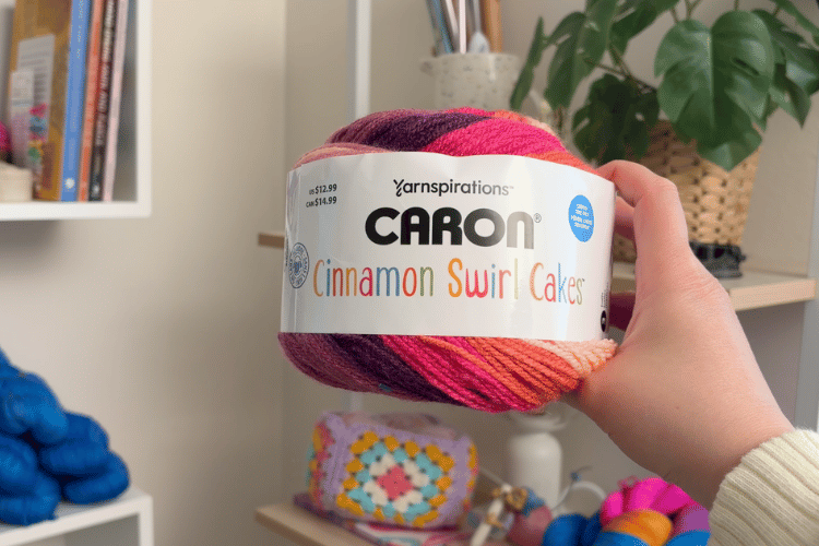image of a woman's hand holding up a skein of caron cinnamon swirl cakes yarn
