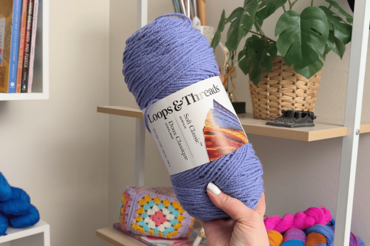 image of a woman's hand holding up a skein of loops and threads soft classic yarn